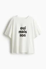 Remera blanca de corte amplio con estampado frontal de la frase "oui mais non" en color negro.