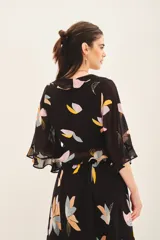 Camisa crop de manga larga con volados en mangas y cintura, confeccionada en viscosa georgette estampada con motivos florales abstractos en tonos pastel sobre fondo negro.