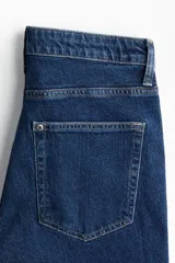 Jean de denim azul oscuro con leve stretch, corte tiro alto y cinco bolsillos. Presenta un corte acampanado desde la rodilla hasta el bajo y costuras verticales marcadas en el frente de las piernas.