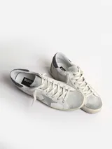 Zapatilla deportiva de cuero blanco con estrella de ante gris y talón con purpurina gris oscuro.