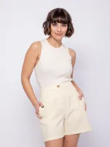Bermuda color crema de algodón, con bolsillos laterales y traseros, y cierre frontal con tres botones veteados. Cuenta con elástico en la pretina trasera.