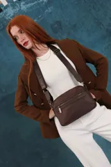 Bandolera color rosa viejo con detalles en cuero marrón claro, múltiples cremalleras metálicas y herrajes plateados. Incluye correa ancha ajustable con el logo de la marca.