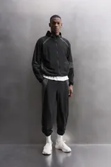 Chaqueta deportiva negra con paneles grises en hombros y laterales, capucha ajustable, cierre frontal con cremallera, bolsillos laterales con cremallera y puños elásticos. Zara Athleticz.