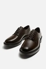 Zapato de vestir tipo derby color marrón oscuro, con parte superior lisa, horma redonda y suela a contraste.