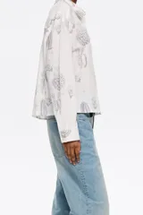 Camisa blanca con estampado de cactus en color gris, corte boxy, cuello camisero, manga larga con puño y cierre frontal con abotonadura.