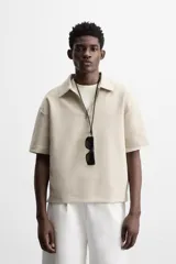 Polo color beige de corte relaxed fit, confeccionado en tejido interlock de algodón con elasticidad. Tiene cuello solapa y cierre frontal de cremallera.