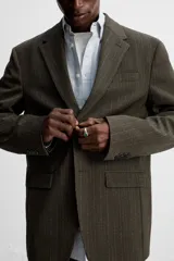 Blazer straight fit color marrón oscuro con finas rayas verticales claras. Confeccionado en tejido con lana de origen italiano. Cuello con solapas de muesca y manga larga acabada en puño con botones. Bolsillos de vivo en pecho y de solapa en cadera. Detalle de bolsillo interior. Bajo con aberturas en espalda. Cierre frontal de botonadura.