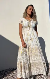 Vestido largo blanco con estampado dorado, escote en V con cordones y mangas cortas abullonadas.