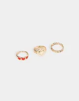Set de tres anillos dorados de metal. Uno con tres corazones rojos esmaltados, otro con un corazón liso y otro con textura.
