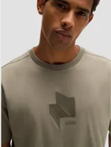 Camiseta negra de corte relajado con cuello redondo y manga corta. Presenta un diseño tridimensional en el pecho que simula un pliegue o estructura geométrica en tono negro brillante o texturizado.