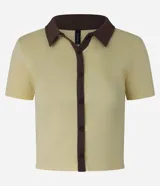 Blusa color amarillo claro confeccionada en tejido rib, con cuello polo marrón, manga corta y cierre frontal con botones marrones.