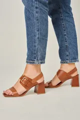 Sandalias de cuero color champagne, con punta cuadrada, tira ancha sobre el empeine y tira al tobillo con hebilla metálica. Taco cuadrado de 7 cm.