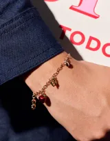 Pulsera dorada de cadena con dijes colgantes: manzana roja, herradura, cuentas doradas y dije ovalado.