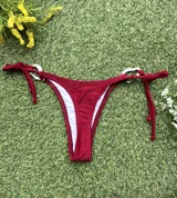 Conjunto de bikini bordó con corpiño triangular con argolla en el centro y bombacha colaless con tiras para atar y argollas en los costados.