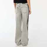 Pantalón de jean gris con lavado ácido y corte holgado. Presenta una franja vertical negra a lo largo de la pierna.
