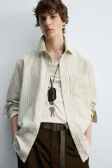 Camisa de hombre relaxed fit confeccionada en tejido de algodón a rayas verticales color beige y marrón. Tiene cuello solapa, manga larga con puños abotonados, bolsillo de parche en el pecho y cierre frontal con botones.