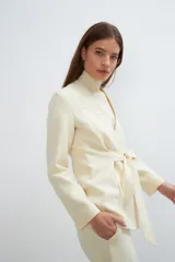 Chaqueta corta entallada color beige, con escote en V, manga larga, cierre frontal con lazo fijo y bolsillos escondidos. Confeccionada en lana fina sin teñir, diseñada exclusivamente por Don Baez.
