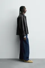 Cazadora de efecto piel color marrón oscuro, corte relajado, con cuello solapa, cierre frontal de botones a presión y bolsillos de vivo en cadera.