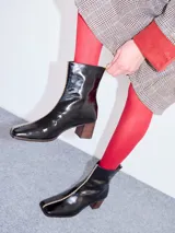 Botas de cuero charol negro con caña media y punta cuadrada. Cuentan con cierre trasero, tirador y bordado contrastante en el empeine. El taco es de madera y la suela de goma.