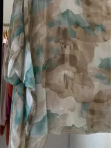 Blusa de seda italiana con estampado abstracto en tonos aqua, marrón y blanco. Tiene cuello redondo y corte asimétrico en el ruedo. Incluye musculosa interior.