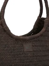 Bolso tipo tote de mimbre trenzado color marrón oscuro, con doble asa superior y parche de cuero con logo de la marca en el frente.