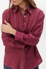 Camisa negra de manga larga con cuello clásico y cierre frontal con botones. Presenta costuras decorativas en color blanco.