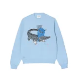 Sweater celeste de corte holgado con cuello redondo y puños y bajo acanalados. Estampado frontal con el logo de Lacoste y un cocodrilo con peluca y collar de perlas, en referencia a la serie Bridgerton de Netflix.