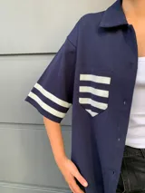 Camisa azul marino de manga corta con rayas horizontales blancas en mangas y bolsillo.