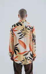 Camisa de manga larga con estampado de hojas en tonos beige, naranja, negro y verde.