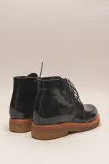 Bota de cuero vacuno con acabado charol, color marrón oscuro. Presenta un diseño de caña corta con cordones frontales y costuras decorativas en la puntera. La suela es de goma tipo crepe.