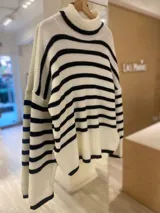 Sweater de punto grueso a rayas horizontales blancas y negras, con cuello alto y mangas largas.