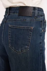 Pantalón de jean azul oscuro de tiro alto, con costuras verticales decorativas en el frente y cierre de botón metálico.