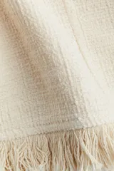 Vestido corto sin mangas color blanco roto, con escote en V pronunciado y textura de tejido bouclé. Presenta costuras moldeadoras en el frente y la espalda, y un bajo con flecos.