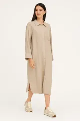 Túnica midi color beige de lino, corte holgado, manga larga, cuello camisero y cierre frontal con botones.