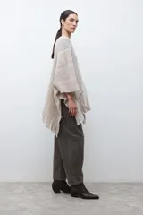 Ruana de tejido de punto en tonos beige y blanco, con patrón de espiga. Presenta cuello en V, mangas amplias, dos bolsillos frontales y flecos en el dobladillo.