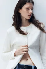 Saco blanco de punto bouclé con cuello redondo, botones forrados hasta la cintura y corte acampanado en la parte inferior.