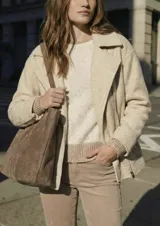 Campera de abrigo color crema, con cuello solapa y cierre frontal asimétrico. Presenta textura bouclé o de lana rizada.