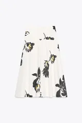 Falda midi de tiro alto confeccionada en hilatura de algodón color blanco con estampado floral en negro y amarillo. Tiene cierre con cremallera oculta en la costura y detalle de botones en la cintura.