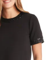 Blusa negra de modal con cuello a la base y espalda con abertura de ojal y botones. Presenta apliques de lentejuelas en el cuello y las mangas.
