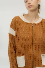 Chaqueta estilo bomber tejida color marrón con detalles en beige, cierre frontal y bolsillos delanteros.