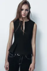 Top color crema, de cuello redondo y sin mangas. Tiene cintura entallada y bajo con pinzas acabado peplum. Cierre frontal con cremallera oculta en costura.
