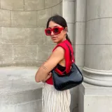 Cartera de hombro negra, estilo baguette, con acabado charol y textura de cocodrilo. Posee correa corta ajustable con detalle de nudo y herrajes dorados.