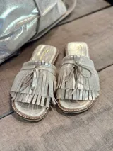 Sandalias bajas color dorado con flecos y lazos decorativos.