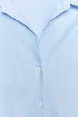 Camisa celeste de corte clásico, con cuello solapa, manga larga, bajo asimétrico y cierre frontal con botones.