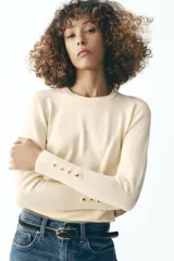 Sweater negro de punto liso con cuello redondo y mangas largas con botones dorados en los puños.
