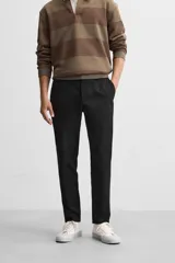 Pantalón negro de corte slim fit, confeccionado en tejido elástico. Cuenta con cintura elástica, bolsillos frontales y traseros de vivo. Cierre frontal con cremallera y botón.
