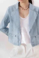 Blazer celeste de denim 100% algodón, entallado y corto a la cadera, con cuello y solapa amplios, mini bolsillos delanteros y bordado con el logo de la marca en el interior del puño.
