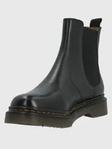 Botín chelsea negro de cuero con elásticos laterales, suela de goma gruesa y pespuntes amarillos alrededor de la suela. Tiene una tira trasera para facilitar el calce.