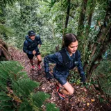 Cortaviento Merrell Skyfire para mujer, con estampado camuflado en tonos azules y negros, cierre frontal con cremallera, capucha ajustable y bolsillo con cierre en el pecho. Logotipo de la marca en color rosa. Ideal para trail running.