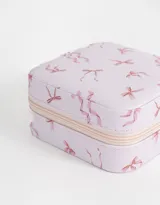 Caja cuadrada porta bijou color lila con estampado de moños rosas y cierre perimetral con cremallera.